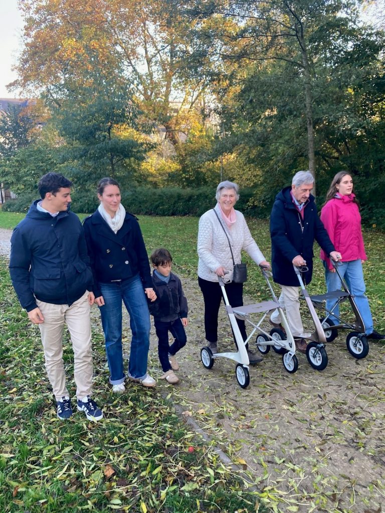 Family walks on autumn path with elders using rollators.